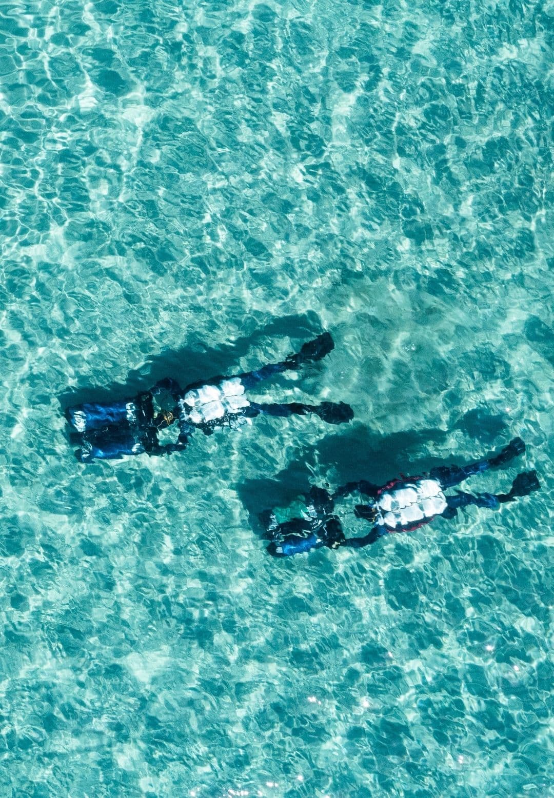 Blick von oben auf zwei Taucher an der Oberfläche über türkisem Wasser